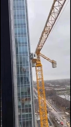 Tower Crane Slams Into High-Rise, Top Section Collapses to Street Below Unspecified City — A routine construction day turned into a terrifying disaster when a tower crane struck the side of a high-rise building, causing its upper section to fail and collapse, sending debris crashing down to the street below. The video shows the yellow crane positioned alongside a glass-clad tower when something suddenly goes wrong near the crane’s top assembly. The jib swings toward the building and makes violen