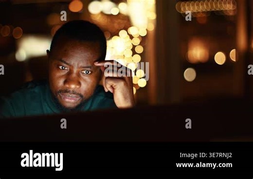 A man with dark skin is engaged with his computer screen in a well-lit office. Twinkling lights create a warm atmosphere, suggesting evening work or study Stock Video Footage - Alamy