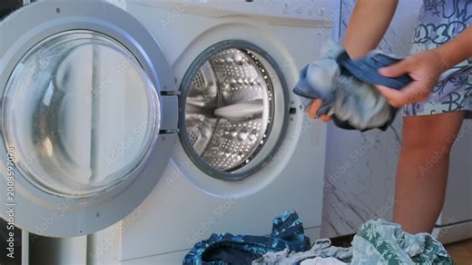 Woman taking clean clothes out of front load washing machine at home. Laundry routine after washing cycle, removing wet garments, domestic chores, hygiene and everyday household maintenance.