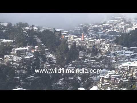 Snow-covered Mussoorie hill station with clock tower and mountain slopes in winter