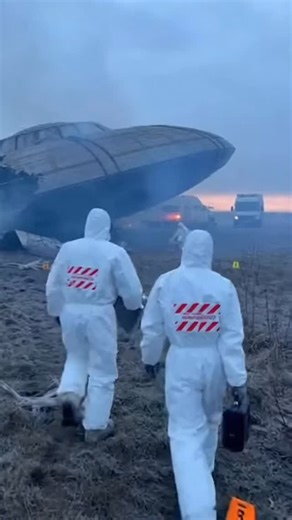 The video shows a restricted area where an alien spacecraft has crashed. The wreckage is visible in the background, partially damaged and surrounded by debris. A group of specially equipped personnel in protective suits enter the perimeter. Two lead officers walk ahead, guiding the team toward the site. The rest follow in a coordinated formation, scanning the area as they approach the fallen craft. this text and video are completely fictional and created using AI. | Светлана Васичкина
