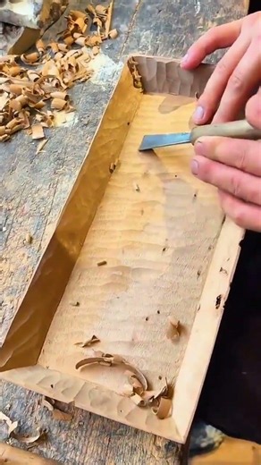 chiseling small ripple patterns on the bottom of a handmade wooden tray using a sharp carving tool