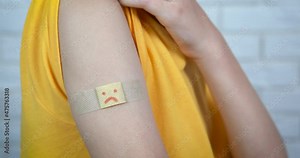 Band aid after vaccination. A view of a band-aid with a sad smile on the child hand after covid vaccination.