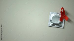 Female hand placing condom with red ribbon, safe sex and AIDS and HIV prevention