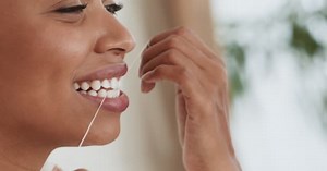 Young black woman flossing her teeth with tooth floss at home, close up portrait