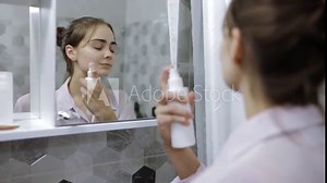 Delighted woman of natural beauty spaying toner and touching soft perfect skin gently while hydrating and moisturizing face and doing daily morning treatment in bathroom