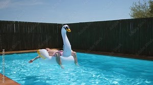 Teen boy relaxes and sunbathe on inflatable swan toy in blue pool