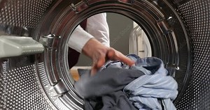 View Looking from the inside Washing machine As the businessman's hands load, take the laundry out of the washing machine. Man in a white shirt is doing laundry.