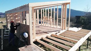 Carpenters hammering nail into OSB panel on the wall of future cottage. Men workers building wooden frame house. Carpentry and construction concept.