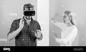 Man VR glasses involved video game while girl try to wake him up. Video game captured imagination of guy. Wife tries to help him back into real life. Video game addiction symptoms and treatment Stock Photo - Alamy