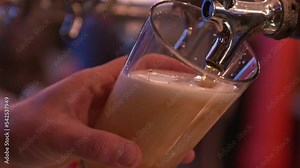 draft beer being poured into a clear glass using a metal draft keg in a dark and busy bar