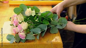 4k A florist girl is packing a bouquet of roses. Flower shop. Step-by-step design of a bouquet of flowers in close-up. March 8th. floriculture, gardening, plants.