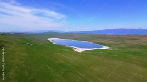 A mountain landscape with blue sky, clouds, green hills, and a beautiful blue mountain salt lake, taken panoramically from a bird's-eye view