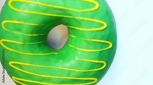 Rotating donut with green confectionery glaze close up, cream frosting and fudge, spinning on light background close up. Sugary and tasty confectionery. Fresh airy donut, sweet buns in bakery shop.