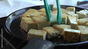Extra firm tofu being cooked and turned on a cast iron pan special ingredients to cook a meal two cans of beans rice plantain avocado red onion and cilantro