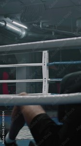 Exhausted African American fighter sits down in boxing ring corner after practice. Male boxer takes off his boxing gloves and takes a break during training. Vertical shot