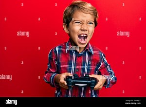 Adorable latin kid playing video game holding controller angry and mad screaming frustrated and furious, shouting with anger. rage and aggressive conc Stock Photo - Alamy