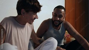 jovem casal gay interracial brasileiro conversando sentados na cama se beijando no dia dos namorados