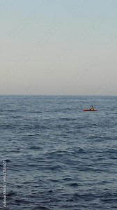 Vertical video of man paddling kayak on ocean water waves in the distance cuts across the shot from right to left