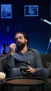 Vertical video Bored gamer gaming on TV console using gamepad, eating popcorn, living sedentary lifestyle. Lazy man in home theatre playing videogames and consuming snacks, sitting on couch, camera B