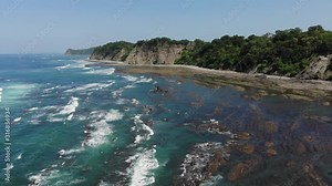 Flyover aerial shot of the rocks at the western side of the Samara bay. Ascending shot, shot at sunny weather. Samara, Costa Rica