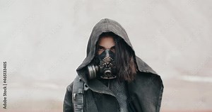 Portrait post apocalyptic human, woman in grunge clothes hooded black mantle protective gas mask respiratory standing in dead desert. Cyberpunk soldier, warrior. Future female survivor after world war