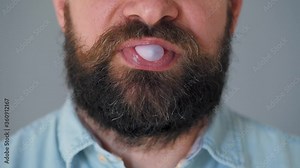 Close-up of a bearded man's mouth chewing chewing gum. Man blowing out a bubble of bubble gum