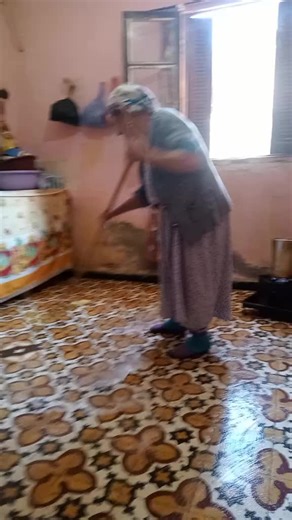 Elderly Woman Cleans Rustic Kitchen Floor with Care