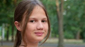 Cute preteen girl face in the park close-up. Face of smiling child looking at camera. Childhood and dreams concept