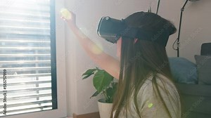 Caucasian girl using VR goggles at home, watching and touching objects in virtual reality, side view.