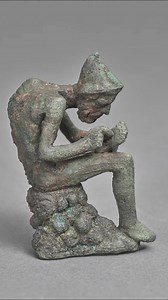 Made over 2000 years ago, this figure of a seated hunchback is attributed to the Hellenistic culture of Alexandria. It is made of bronze and depicts a compact, expressive seated figure. It measures 8.9 x 6.7 x 5 cm (3.5 x 2.63 x 1.97 in). This artifact is now housed at the Wadsworth Atheneum Museum of Art in Hartford, Connecticut, United States. It was acquired as a gift from J. Pierpont Morgan. | Cosmos University