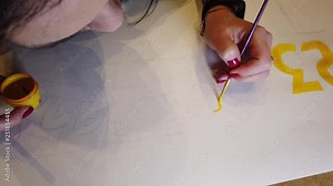 Pretty young lady is busy painting picture in workshop using bright paint and stained palette.