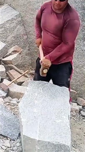 hitting the large grey stone surface using a long handled metal hammer with a lot of rubble around