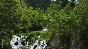 Aerial dolly shot of the upper Roughlock Falls showcasing the rushing water in Spearfish Canyon, South Dakota behind beautiful green summer leaves.