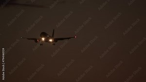 Airplane with bright landing lights approaches in a dark sky, wingtip navigation lights visible