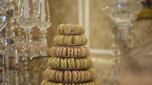 A delicate tower of pastel-colored macarons on a dessert stand, with a backdrop of sparkling chandeliers and luxurious decor. The macarons in soft shades of yellow and pink are arranged