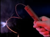 Fuse being lit on stick of dynamite being held in hand / flame goes...