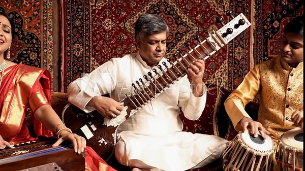 Indian Classical Music Performance - A group of three Indian musicians perform classical music. One plays the sitar, another plays the tabla drums, and a third sings and plays the harmonium.
