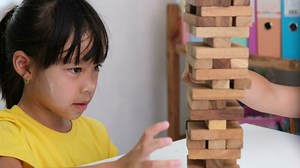 Cute Asian siblings having fun playing Jenga together. Two children playing Jenga board game on table in room at home. Wooden puzzles are games that increase intelligence for children.