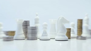 White chess pieces on a white background. Chess game. Pawn. Rook. Knight. Bishop. Silver and gold stack of metallic coins.