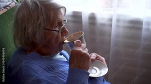 Old lady drinking tea while sitting next to the window
