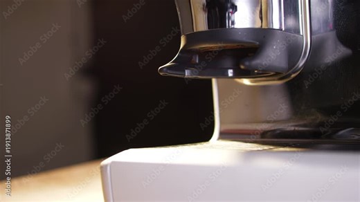 Close up of a barista removing a black handled portafilter from an automatic espresso grinder after dosing fresh coffee grounds. Clean motion and reflective metal surfaces highlight workflow and brewi