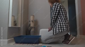 Senior woman assembles new cat litter box together with pet at home. Elderly female playing with cat sets hooded litter box for pet to go to toilet. Pet care, hygiene concept. Hooded cat litter pan.