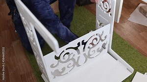 A man is assembling a plywood computer desk. Connects shelves and racks. Aligns grooves and holes. Installs fasteners.