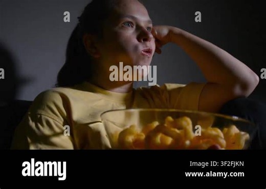 Young woman sitting on a sofa and eating corn rings while watching a movie. Cozy home entertainment scene focused on snacking, relaxation and leisure Stock Video Footage - Alamy