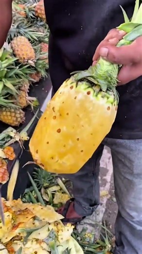 Peeling a fresh yellow pineapple using a sharp knife to remove the skin and eyes with precision