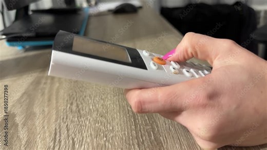 Person Adjusting Settings On Small Device, Homeowner Presses Buttons On Remote Over Wooden Table