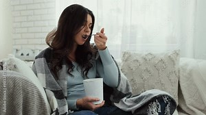 Stress eating concept. Upset lady eating ice cream and crying under warm plaid at home, going through breakup, having broken heart