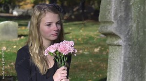 Sad young girl sitting in front of tombstone at graveyard.