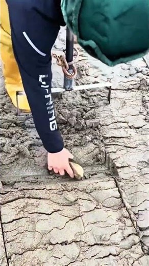 Yellow waterproof pants brace muddy shore, pole sinks deep with chain’s pull